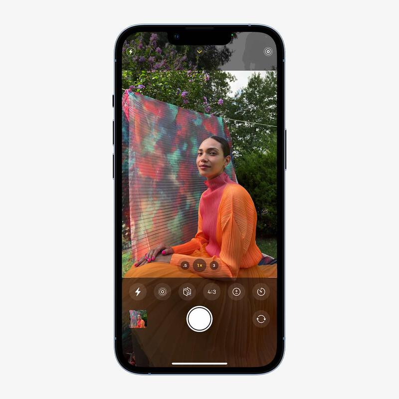 The iPhone 13 camera interface displays a subject with photography controls for outdoor shooting