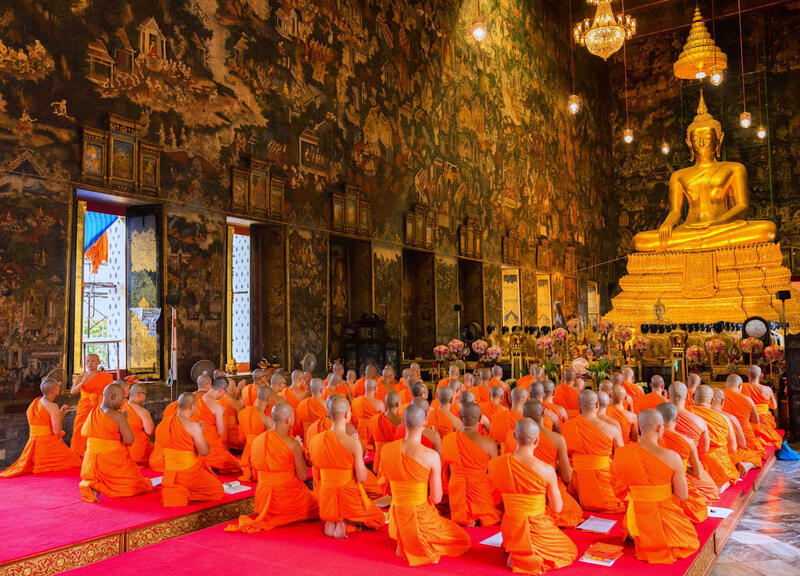 Buddhist monks in orange robes praying inside a decorated temple during Thai Buddhist Lent Day ceremony