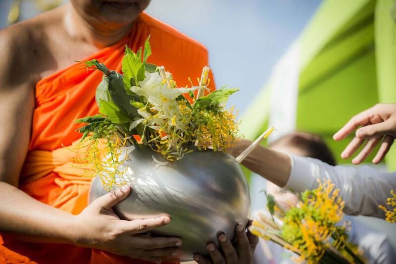 A Buddhist monk receiving traditional flower offerings in a silver bowl during a religious ceremony