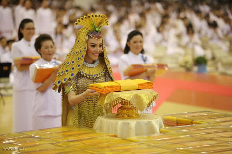 A woman in traditional Thai costume offers a saffron robe during the Kathina Buddhist ceremony