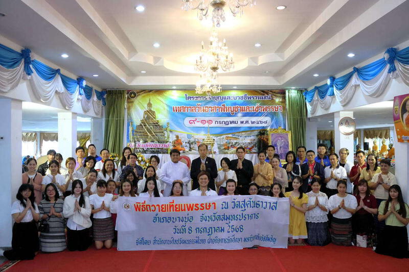 Group photo at a Thai Buddhist candle offering ceremony event held on 8th July 2568, showing participants in traditional and modern attire with a ceremonial banner